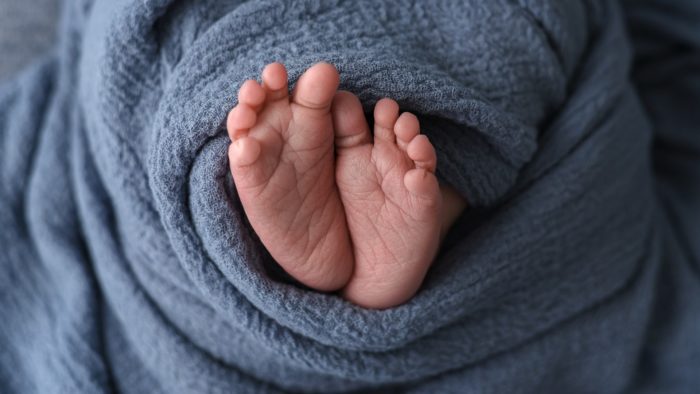 Zu sehen sind mittig zwei kleine Babyfüße in ein blaue Decke eingewickelt.