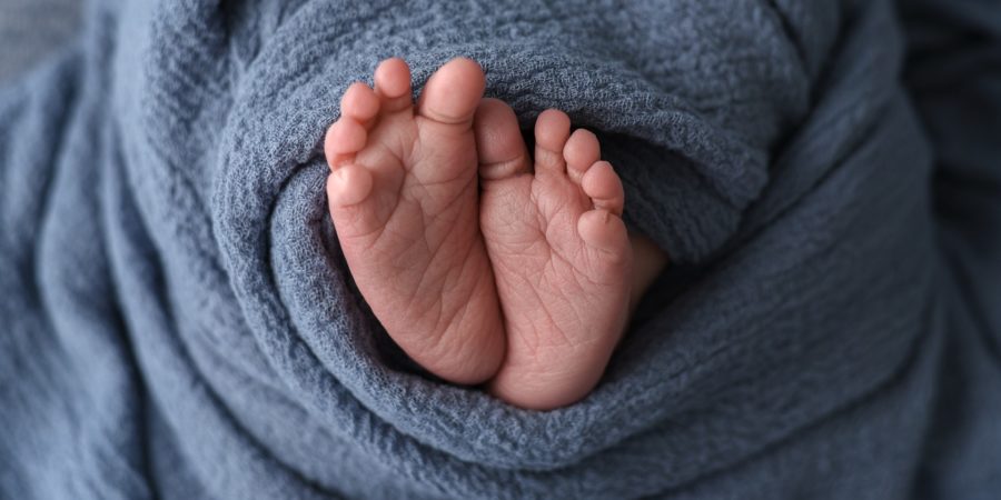 Zu sehen sind mittig zwei kleine Babyfüße in ein blaue Decke eingewickelt.